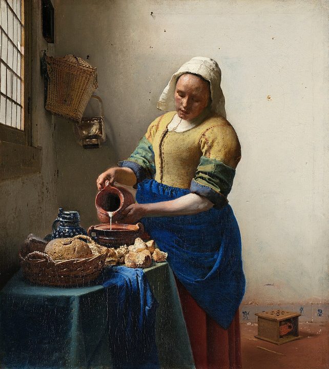 A maid pouring milk at a table, lit by daylight from a window on the left